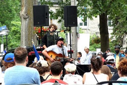 Photo caption: On June 24, hundreds of people hit the streets of rue Principale to celebrate St-Jean Baptiste Day, as Quebec singer songwriter Émile Bilodeau performed songs from his 2019 album Grandeur Mature on the back of a roaming pickup truck. Pictured, Bilodeau entertains the crowd with a rendition of “Métaphores” next to the Parc Commémoratif in the afternoon. Photo: J-D Potié